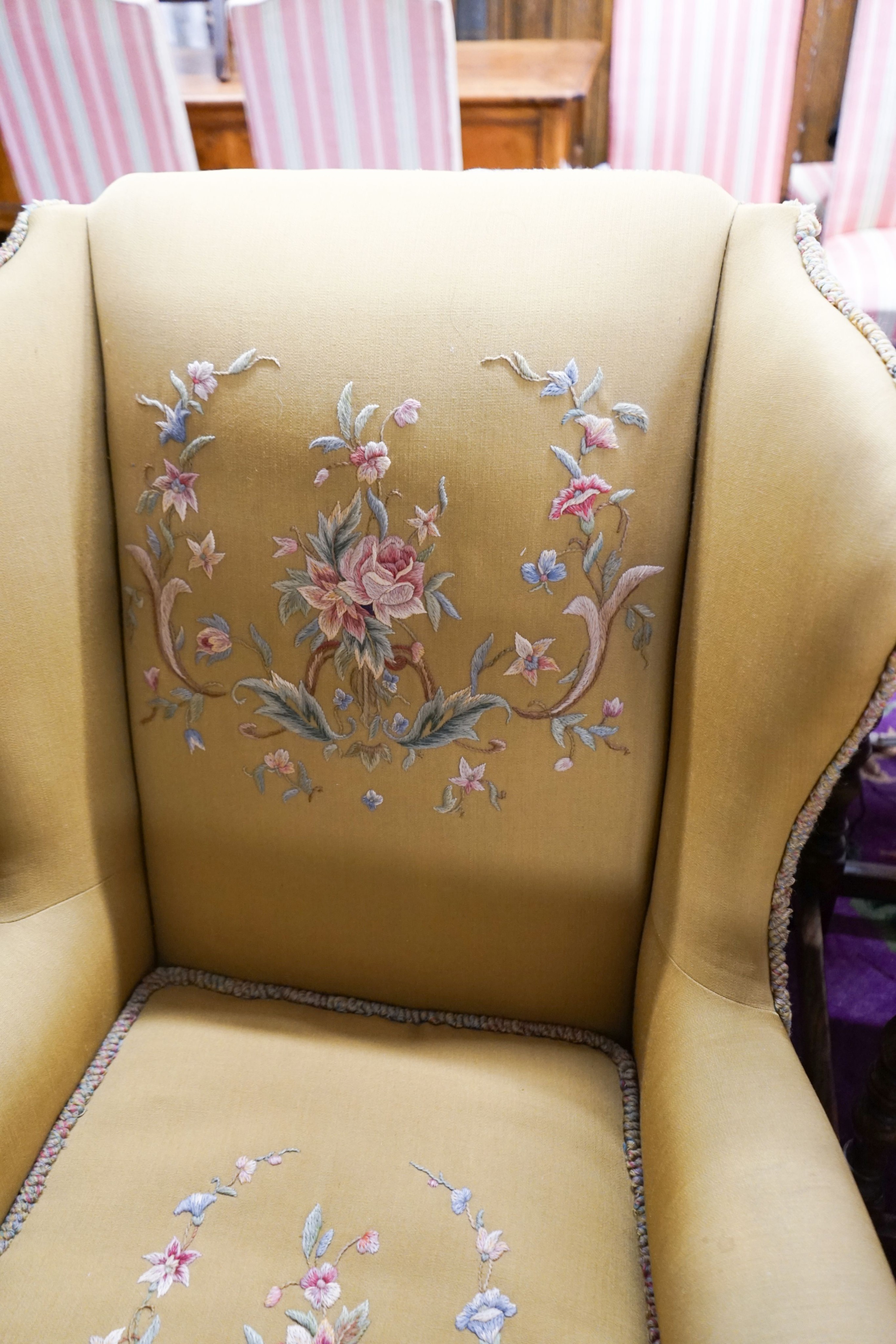 A wing frame armchair, upholstered in gold with embroidered flowers, on carved lion’s paw feet, width 80cm, depth 80cm, height 102cm